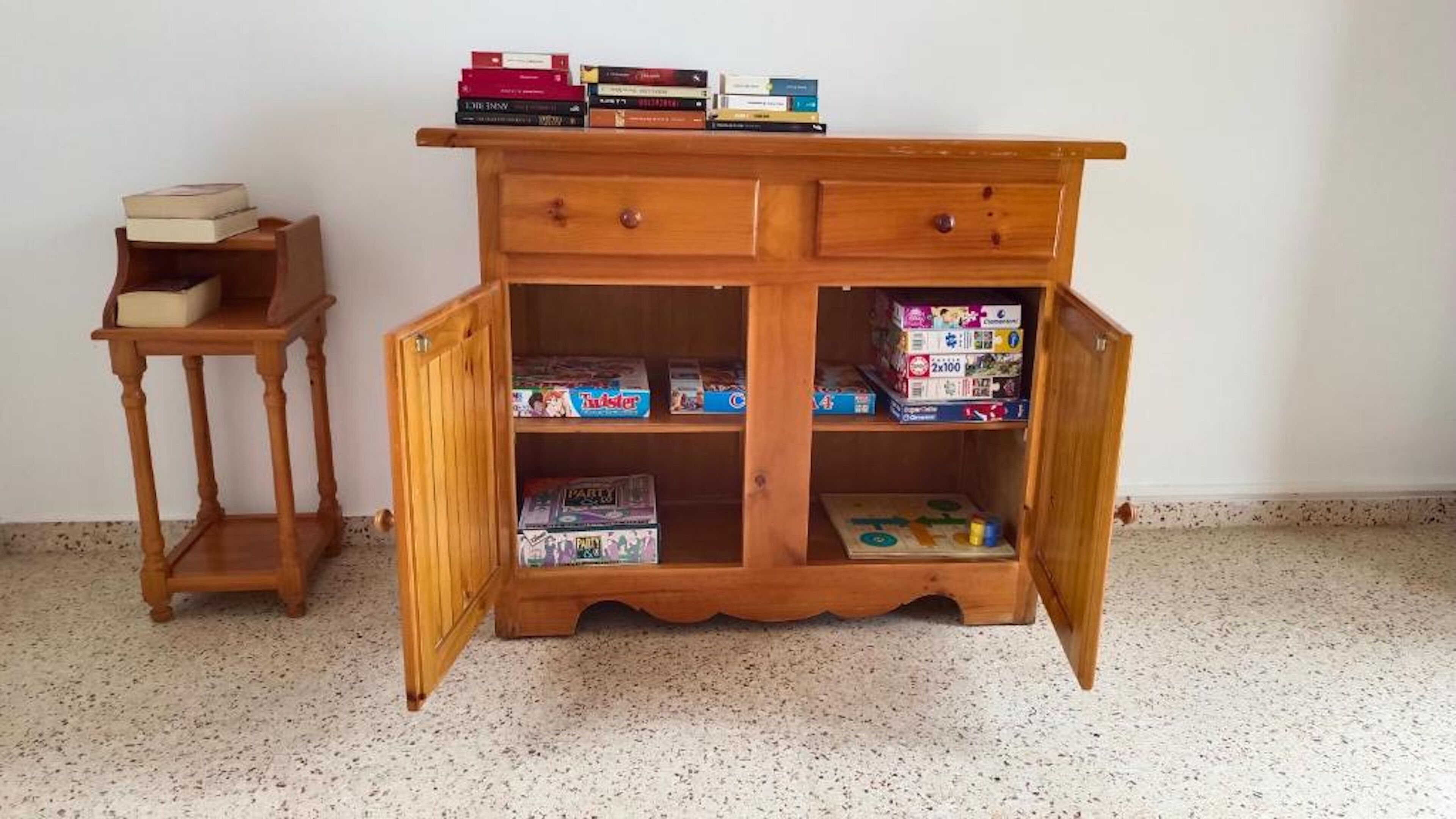Een houten kast met open deuren, waar spelletjes en een klein tafeltje bij staan.