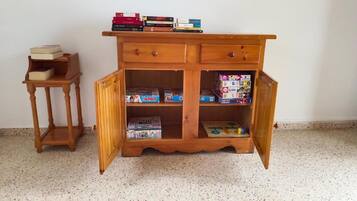 Een houten kast met open deuren, waar spelletjes en een klein tafeltje bij staan.