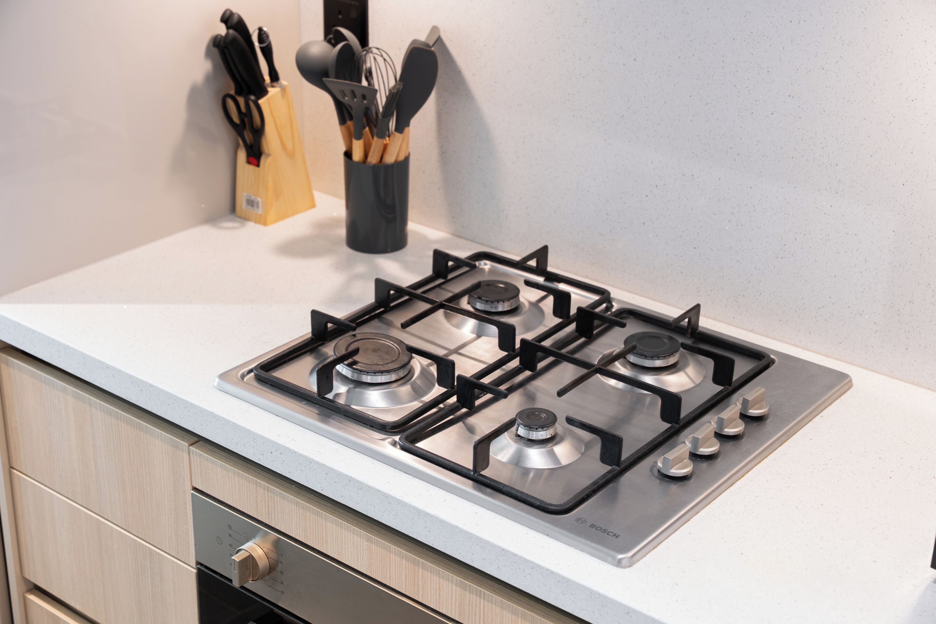 A kitchen with a four-burner gas stove, a wooden utensil holder, and a Bosch brand gas stove.