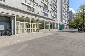 Ein mehrstöckiges Gebäude mit Eingangsbereich im Erdgeschoss, großen Fenstern und einer gepflasterten Fläche, auf der Fahrräder abgestellt sind.