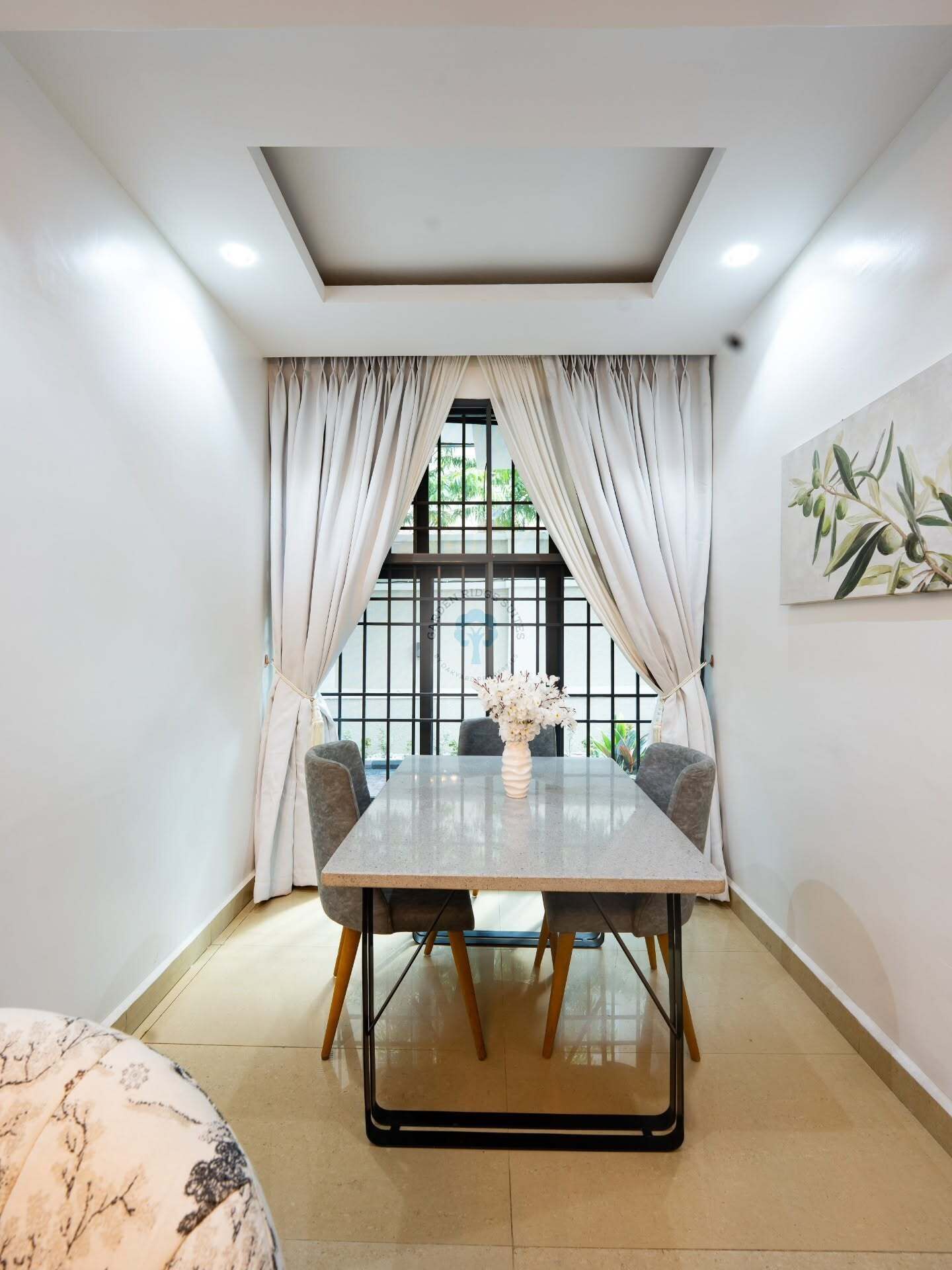 Uma sala de jantar moderna com uma mesa retangular, duas cadeiras, um vaso com flores e uma janela com cortinas.