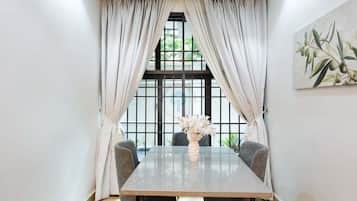 Un comedor moderno con una mesa rectangular, dos sillas, un florero con flores y un ventanal con cortinas.