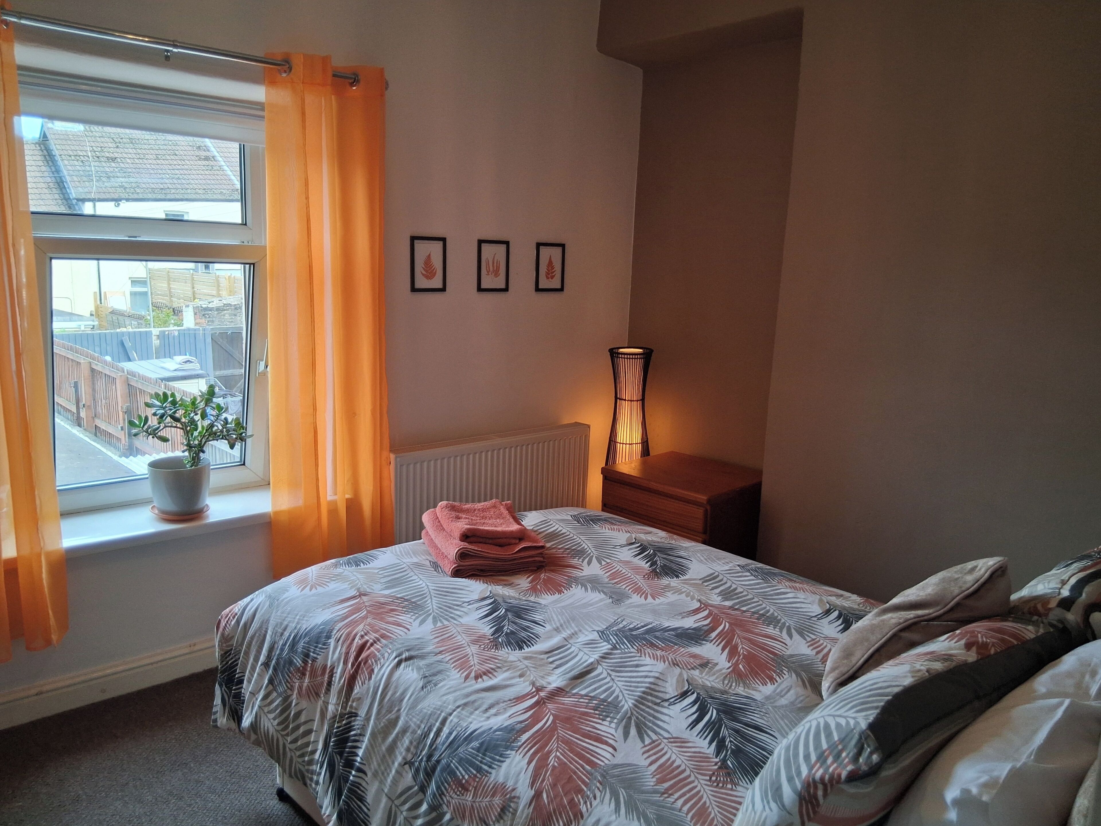 A bedroom with a bed, a window with curtains, a radiator, and a bedside table with a lamp.