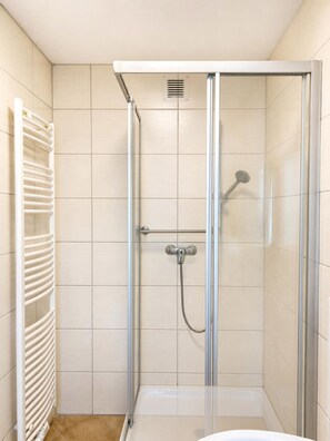 Eine Duschkabine mit Glastür, Handbrause und am Wand montierter Armatur.