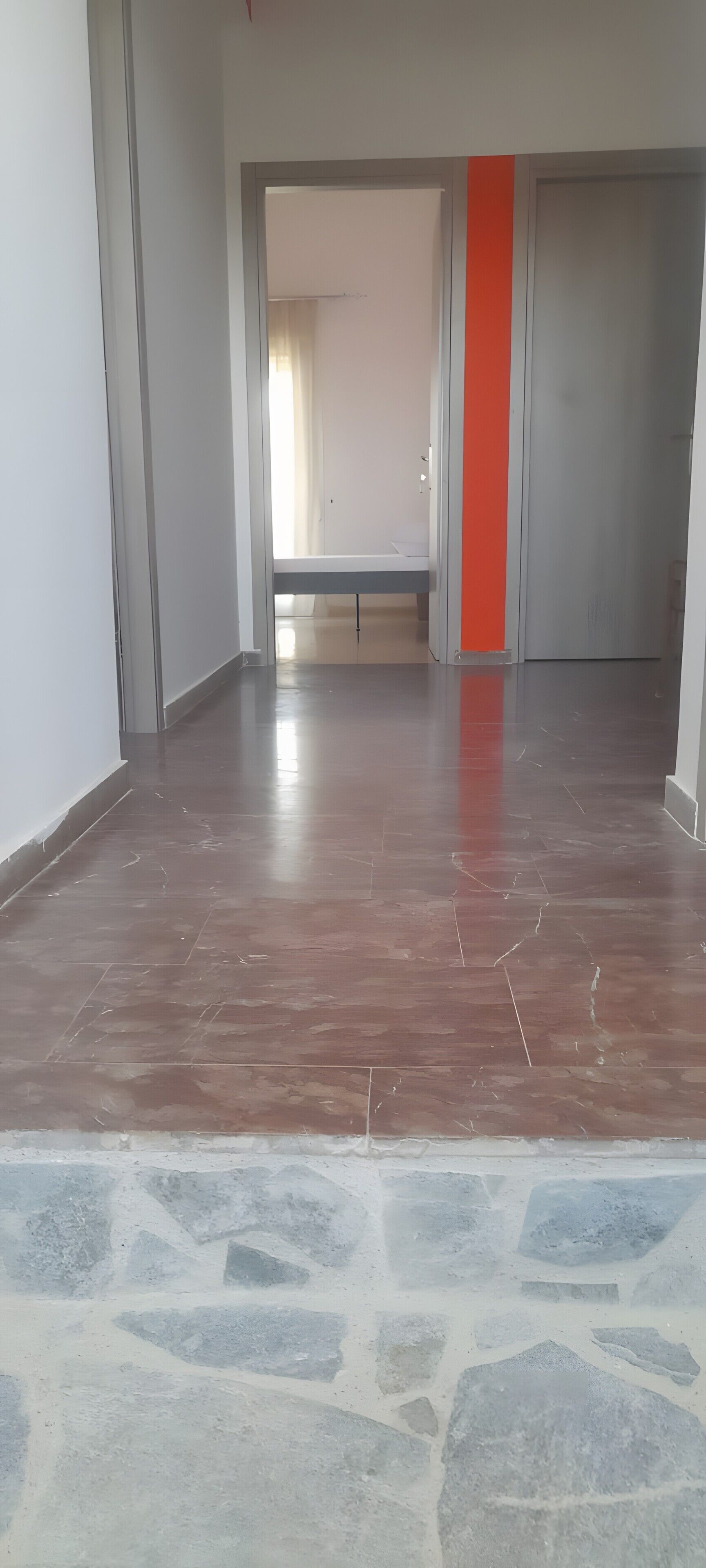 A spacious room with a tiled floor, a bench, and a door with a red accent.