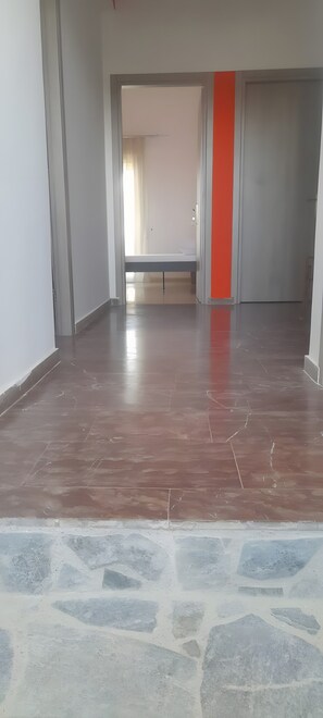 A spacious room with a tiled floor, a bench, and a door with a red accent.