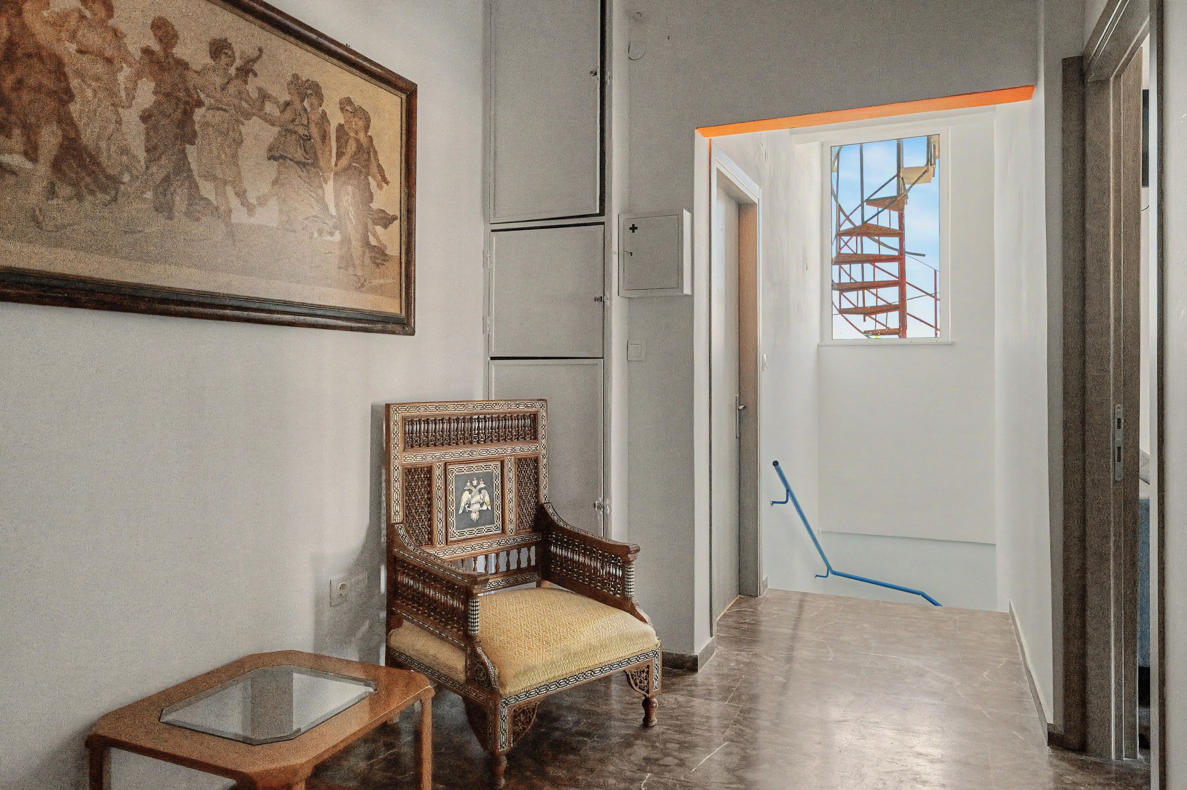A hallway with a wooden chair, a framed picture on the wall, and a door with scaffolding outside.