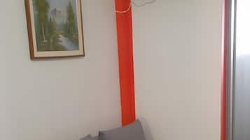 Een kamer met een grijze bank, een schilderij, een rode zuil en een flatscreen televisie aan de muur.