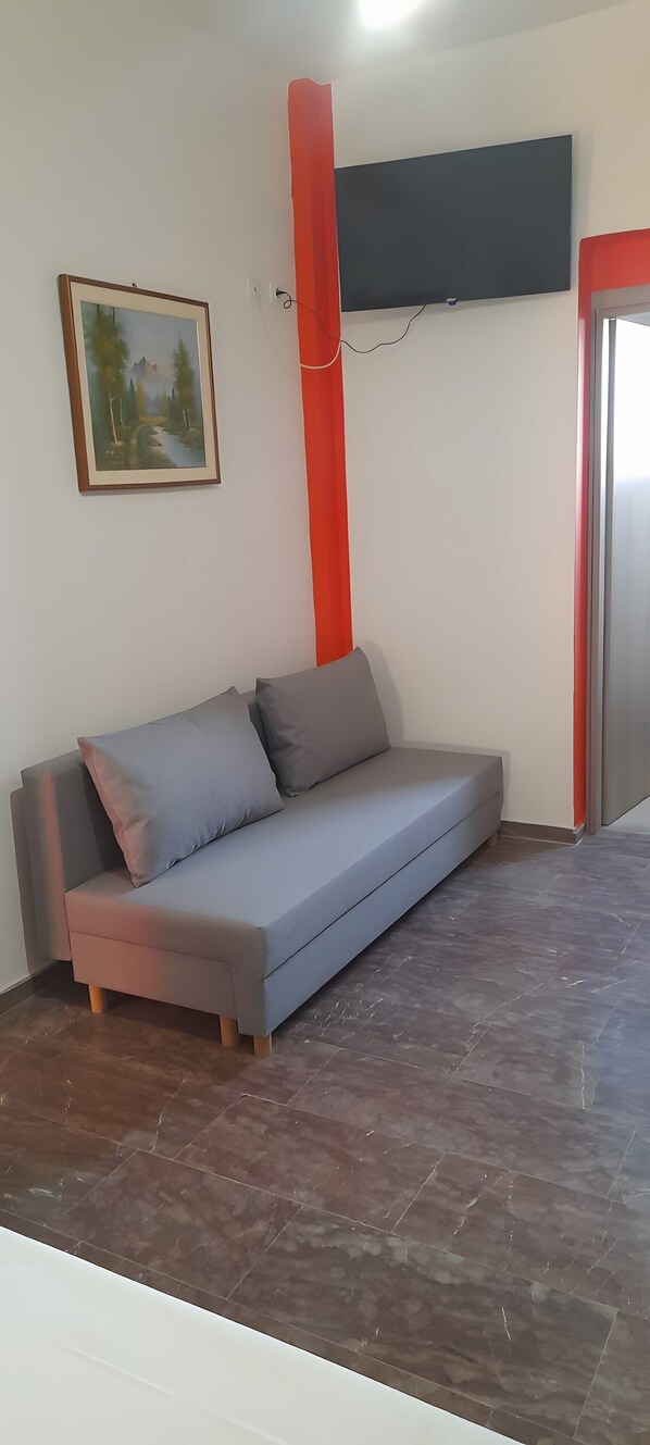 A room with a grey sofa, a painting, a red pillar, and a flat-screen TV mounted on the wall.