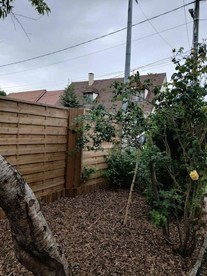 A backyard with a wooden fence, a tree, and a garden bed covered with mulch. - A quiet house within a 15-minute walk of the train station, close to Disney and Paris (Lagny-sur-Marne)