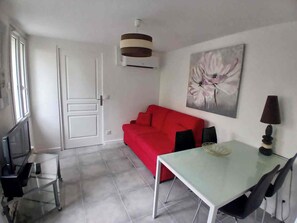 Ein gemütlicher Wohnraum mit einem roten Sofa, einem Glastisch, einem Fernseher und einem Bild an der Wand.
