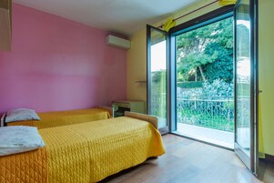 Una habitación con dos camas, un escritorio y un ventanal corredera que da a un balcón.