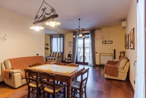 Amplia sala de estar con una mesa de comedor de madera, un sofá y una silla. Un candelabro cuelga del techo.