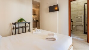 A hotel room with a bed, a TV mounted on the wall, a small table with chairs, and a bathroom visible through an open door. - Cloud Swing Room 1 by Wonderful Italy (Bari)