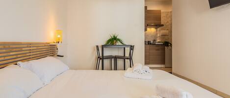 A hotel room with a bed, bedside table, lamp, and a view into the kitchen area.