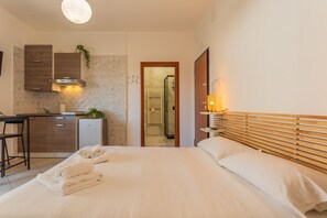 Ett hotellrum med en säng, ett skrivbord, ett litet kök och ett badrum som syns genom en öppen dörr.