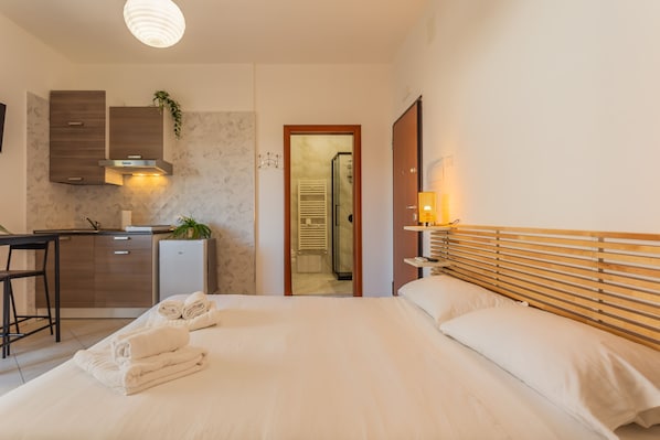 Ein Hotelzimmer mit Bett, Schreibtisch, einer kleinen Küche und einem durch eine offene Tür einsehbarer Badezimmer.