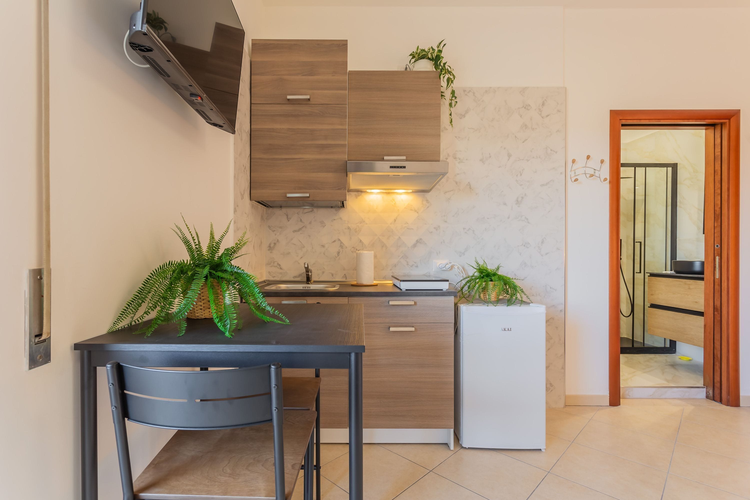 Une cuisine compacte équipée d’une cuisinière intégrée, d’un évier et d’un réfrigérateur. On y trouve deux chaises et une table agrémentée de plantes.