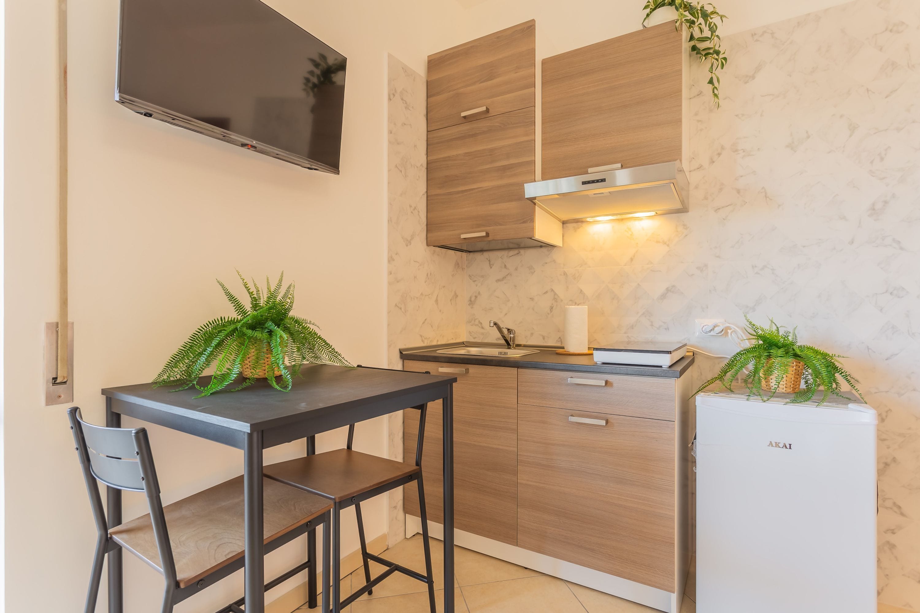Une cuisine de taille réduite avec une table sombre, deux chaises, un four encastré et un téléviseur fixé au mur.