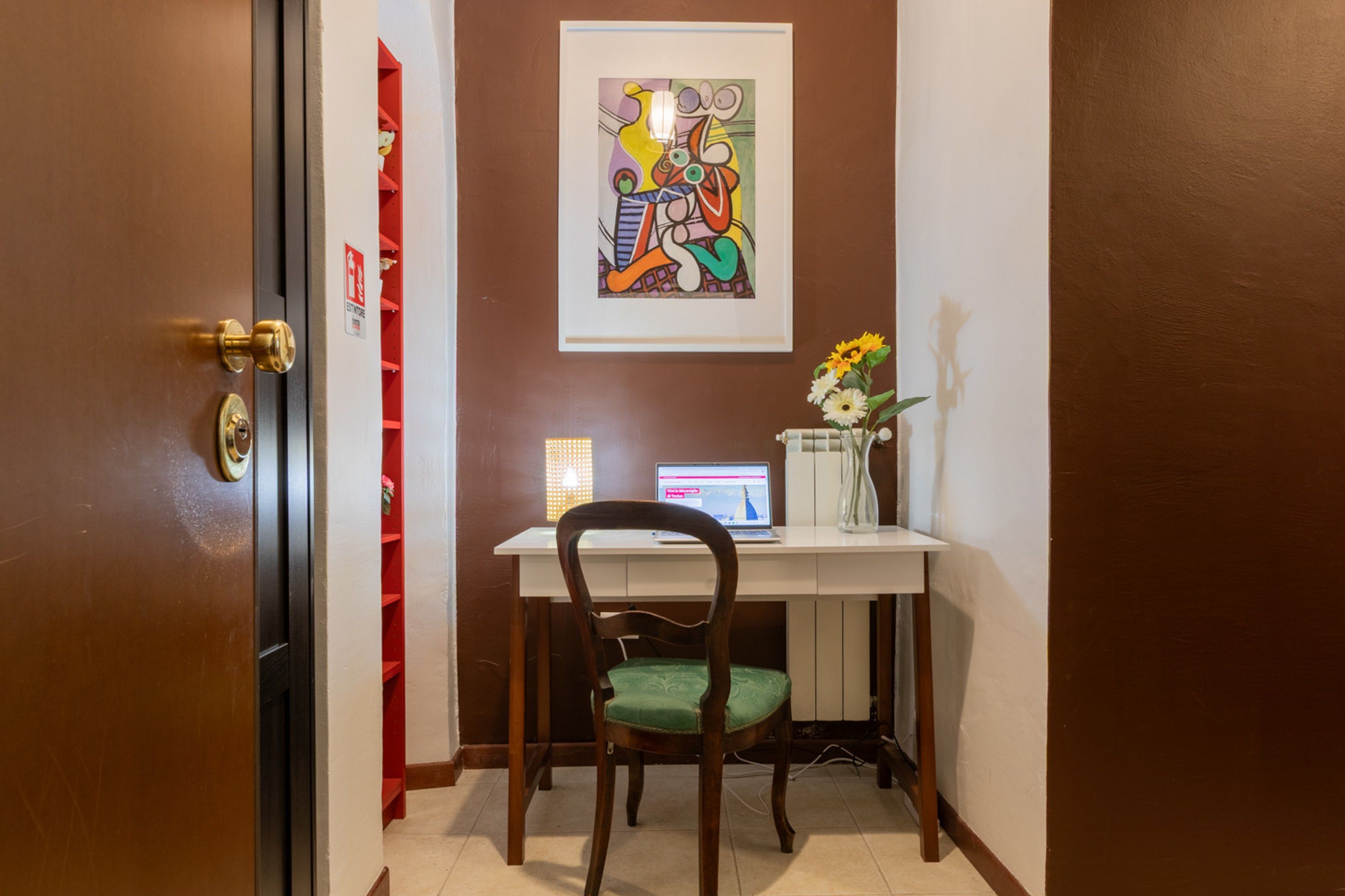 A room with a desk, chair, and a framed abstract painting on the wall.