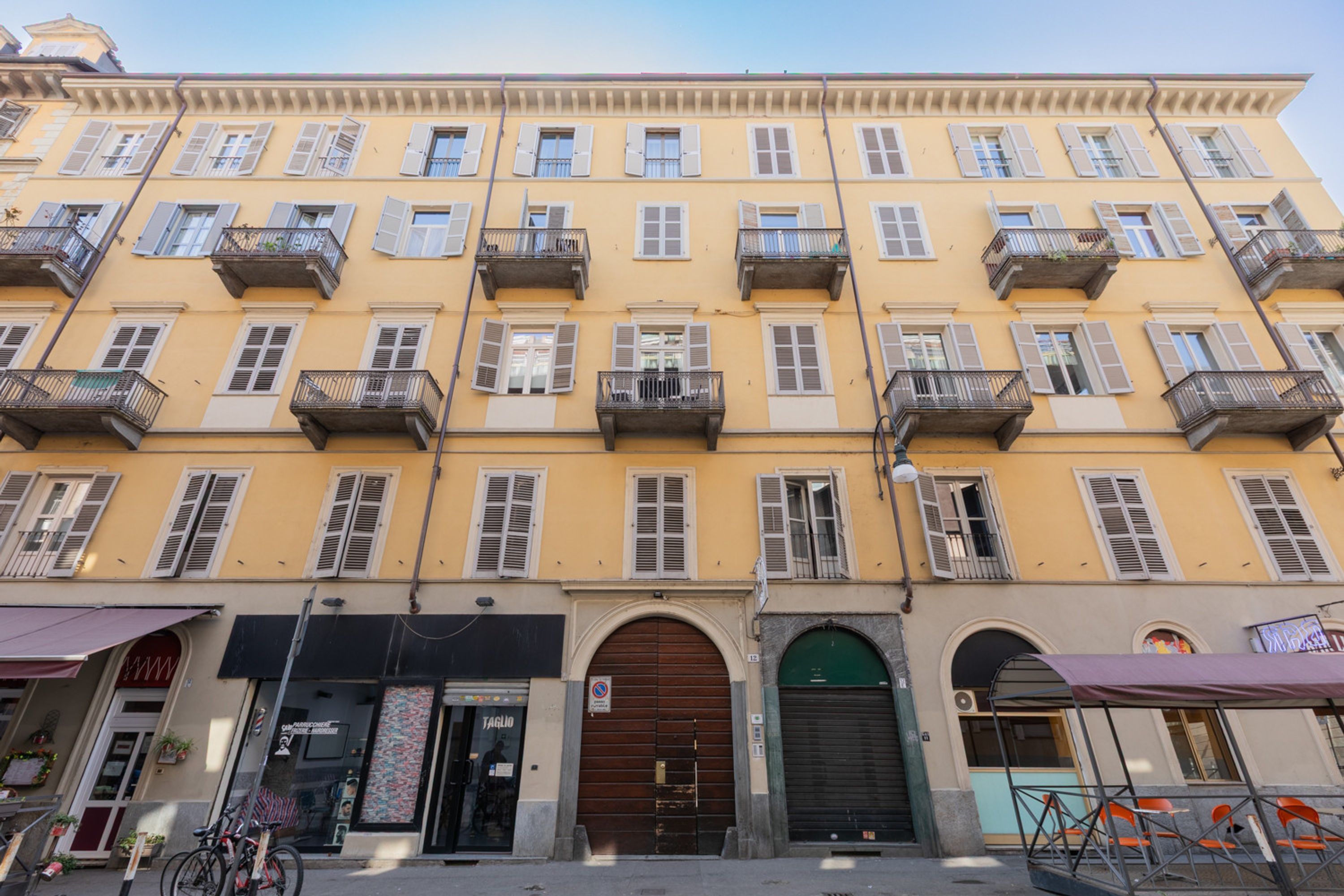 A multi-story building with balconies, a ground-level entrance with a door, and a storefront with a sign.