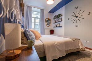 A bedroom with a bed, a bedside table with a lamp, a clock on the wall, and a window with curtains. - Casa Tropicana Ro-jo by Wonderful Italy (Turin)