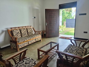 A room with a wooden sofa and matching chairs, a glass coffee table, and a door leading outside. - Lashi Dreams Ahangama (Ahangama)