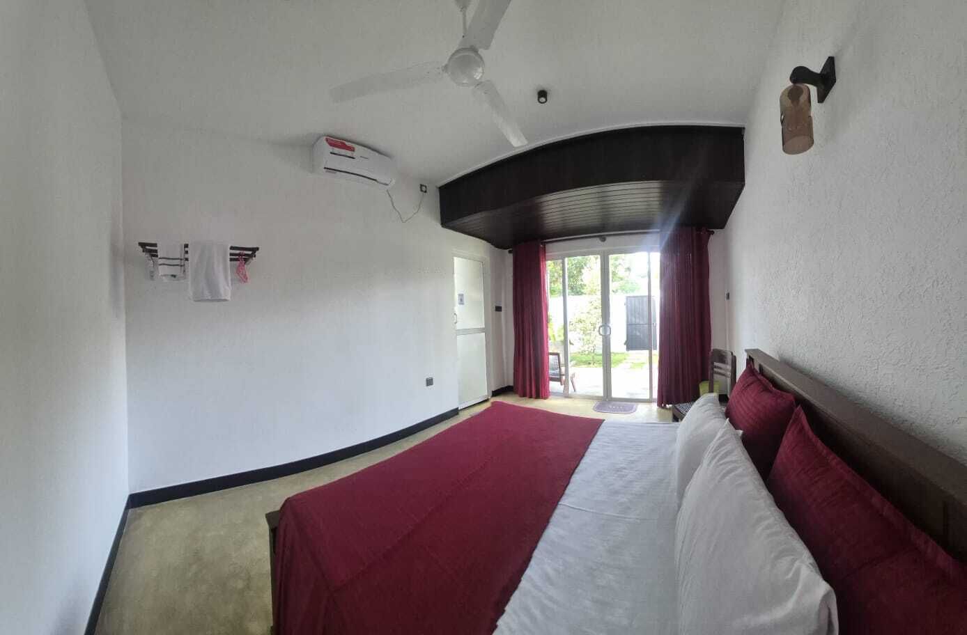 Et hotelværelse med seng, ventilator, et vindue med gardiner og en dør til en balkon.