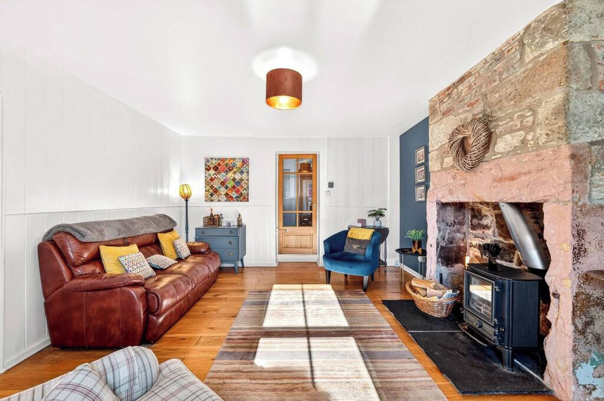 A cozy living room with a leather sofa, a blue armchair, and a stone fireplace.