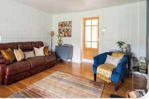 Una sala de estar con un sofá de cuero marrón, un sillón azul y piso de madera.