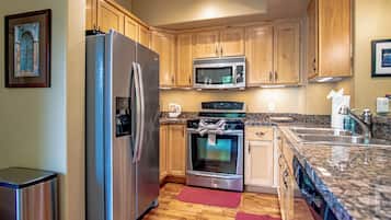 A modern kitchen with stainless steel appliances, wooden cabinets, granite countertops, and a red rug.