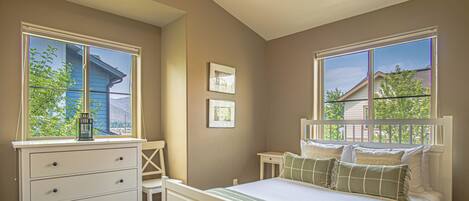 A bedroom with a bed, a desk, and two windows.