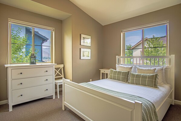 A bedroom with a bed, a desk, and two windows.