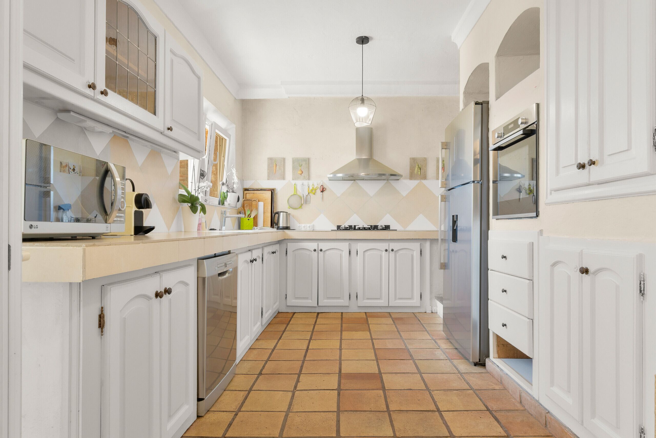 A kitchen with white cabinetry, a tiled floor, and a stainless steel range hood.