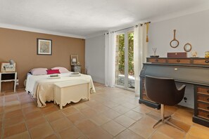 Een slaapkamer met een bed, nachtkastjes, een kaptafel en een stoel. Er is een raam met gordijnen en uitzicht op groen.