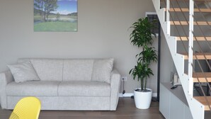 A modern interior with a wooden ceiling, a grey sofa, a yellow chair, a staircase, and a potted plant. - Onga Apartment with a Stunning View of the Euganean Hills (Veneto)