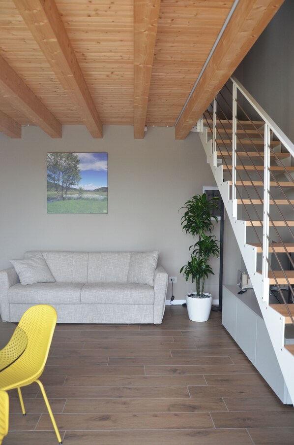 A modern interior with a wooden ceiling, a grey sofa, a yellow chair, a staircase, and a potted plant.
