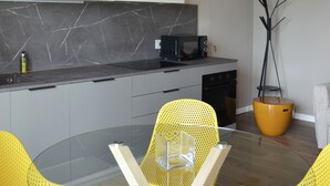 A modern kitchen with a glass dining table, yellow chairs, and a black microwave. - Onga Apartment with a Stunning View of the Euganean Hills (Veneto)