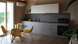 A modern kitchen with a glass dining table and chairs, a built-in oven, and a view of the outdoors. - Onga Apartment with a Stunning View of the Euganean Hills (Veneto)