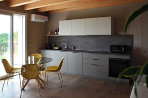 A modern kitchen with a glass dining table and chairs, a built-in oven, and a view of the outdoors. - Onga Apartment with a Stunning View of the Euganean Hills (Veneto)