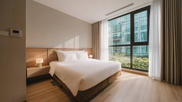 Une chambre d’hôtel moderne avec un grand lit, une table de chevet, un thermostat fixé au mur et une vue sur un immeuble par une grande fenêtre.