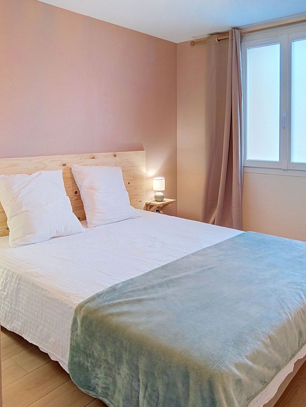 A bedroom with a bed, a nightstand with a lamp, and a window with curtains.