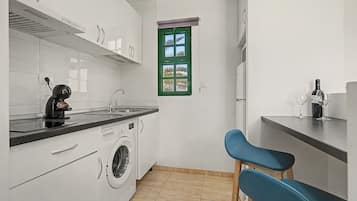 A compact kitchen with a washing machine, a coffee machine, and a window with a green frame.