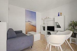 Ett modernt vardagsrum med en grå soffa, en vit fåtölj, en platt-TV och en bokhylla.