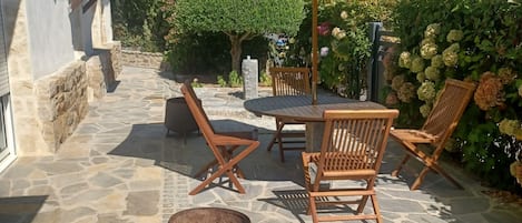 En terrasse med stenbelægning, træmøbler og en gul parasol.