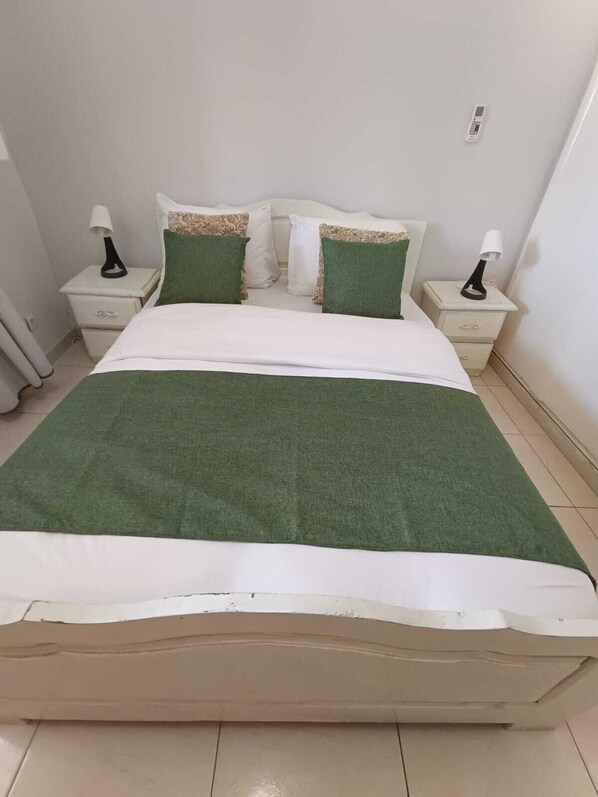 Ein Bett mit grüner Bettdecke, weißen Kissen und zwei Nachttischen mit Lampen.