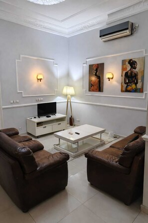 Ein modernes Wohnzimmer mit zwei Ledersofas, einem weißen Couchtisch, einem Fernsehgerät auf einer weißen Kommode und Wandbildern.