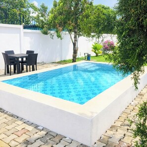 Una piscina rettangolare con un motivo piastrellato, circondata da un muro bianco e da un patio lastricato con tavolo e sedie.
