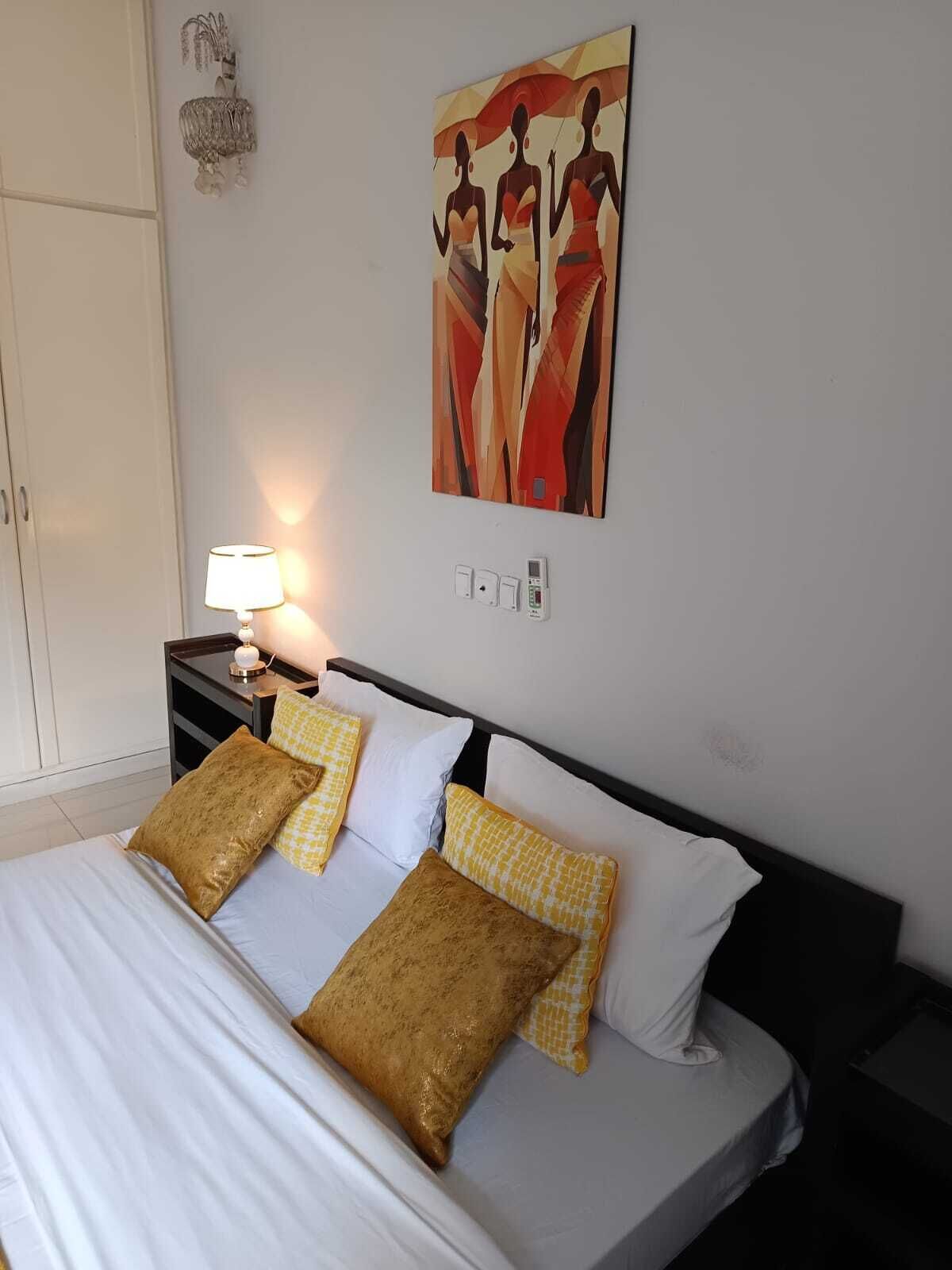 Een hotelkamer met een bed, nachtkastje met een lamp, wandkunst en een kledingkast.
