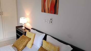 Een hotelkamer met een bed, nachtkastje met een lamp, wandkunst en een kledingkast.